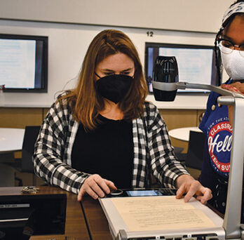 A classroom support student assists an instructor with the use of the overhead projector. 