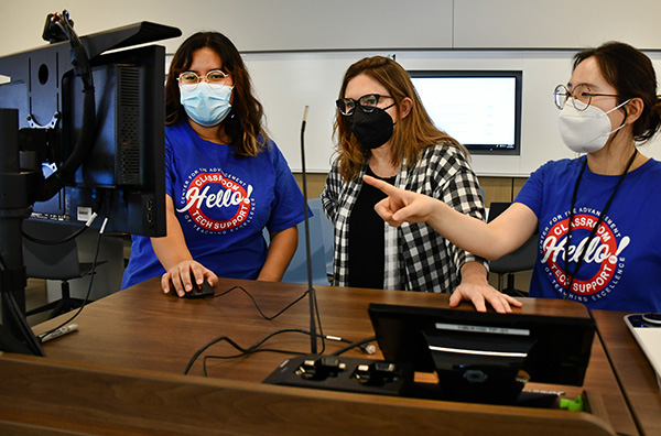 Two classroom support students help an instructor set up her lecture in a smart classroom podium.