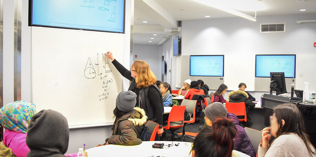 Martina Bode writes on a whiteboard, helping a group of students during an in-class active learning session.
