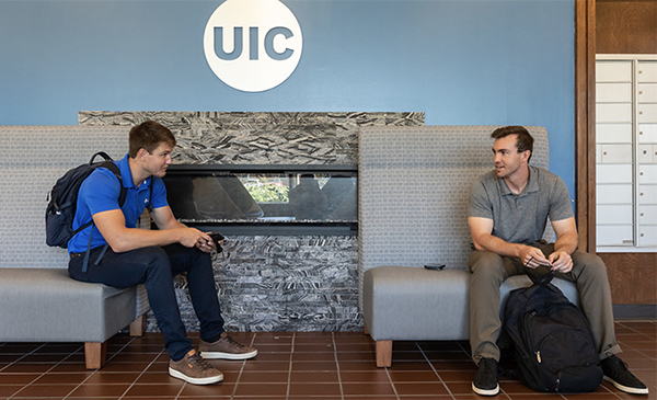 Two UIC students without masks sit indoors and talk, keeping a socially appropriate distance of five feet between them.