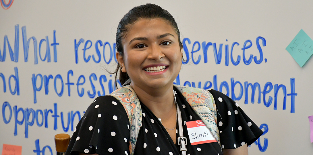 A young women smiles radiantly. Her name tag reads 