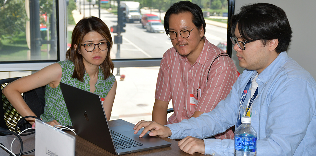 A man on a laptop shows another man and a woman what he is doing on the screen.