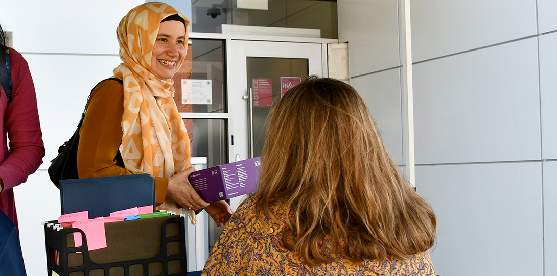 a young, smiling woman wearing a headscarf takes a name tag from a woman sitting at a registration table.
